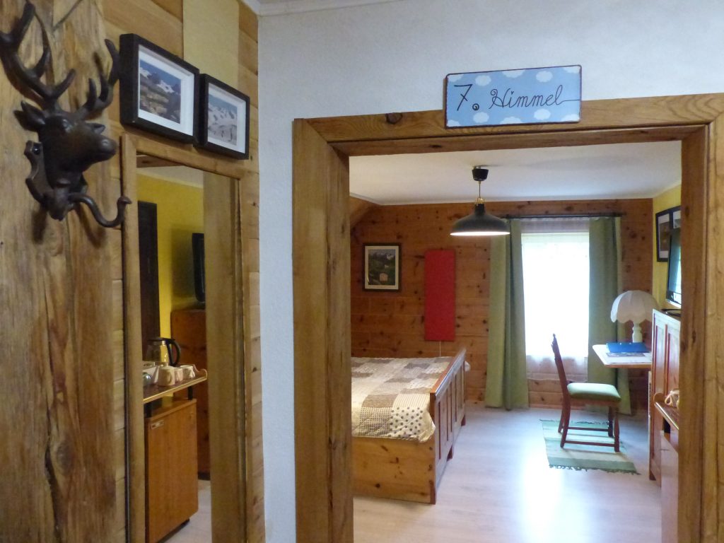 Blick durch den Türrahmen ins Walde-Zimmer mit Holzvertäfelung, Bett, Schreibtisch am Fenster, Fernseher und rotem Infrarotpanel an der Wand.