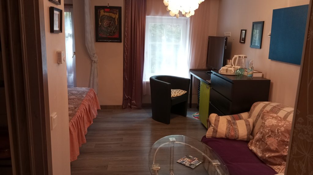Junior Suite „Hundertwasser“ mit Bett, Schreibtisch, Sessel, Kommode mit Teetablett und großem Fenster.